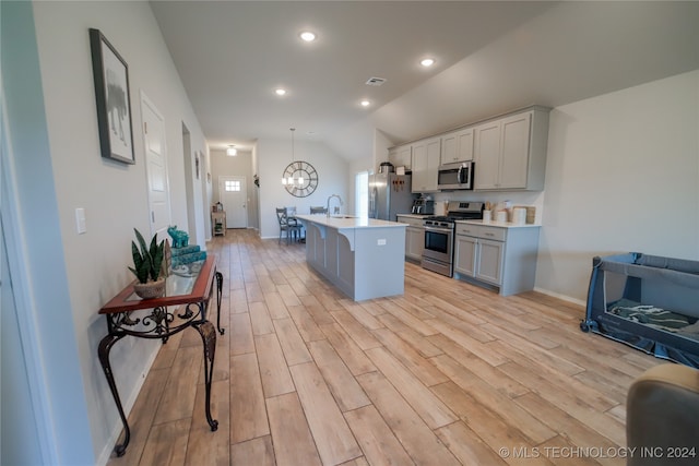 kitchen featuring lofted ceiling, stainless steel appliances, sink, a kitchen island with sink, and a breakfast bar