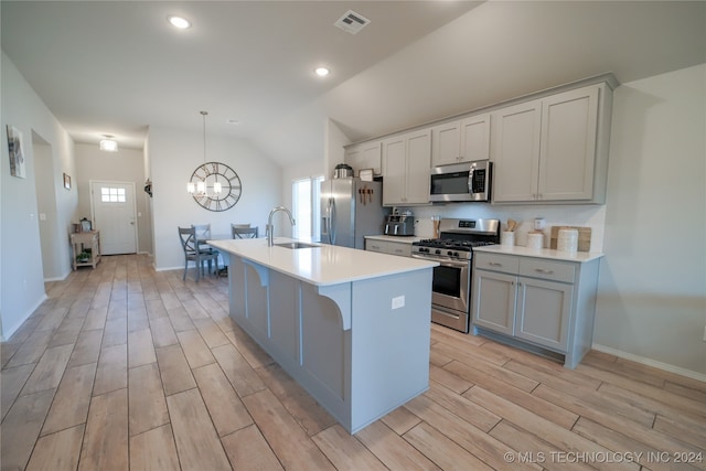 kitchen with appliances with stainless steel finishes, lofted ceiling, sink, a kitchen island with sink, and a chandelier