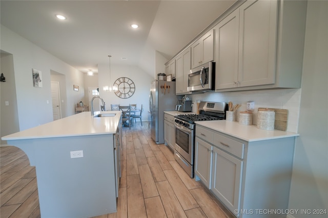 kitchen with a center island with sink, gray cabinets, appliances with stainless steel finishes, decorative light fixtures, and lofted ceiling