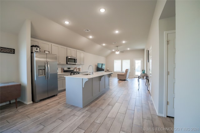 kitchen featuring ceiling fan, vaulted ceiling, appliances with stainless steel finishes, an island with sink, and a kitchen breakfast bar