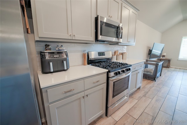 kitchen with vaulted ceiling, appliances with stainless steel finishes, and decorative backsplash