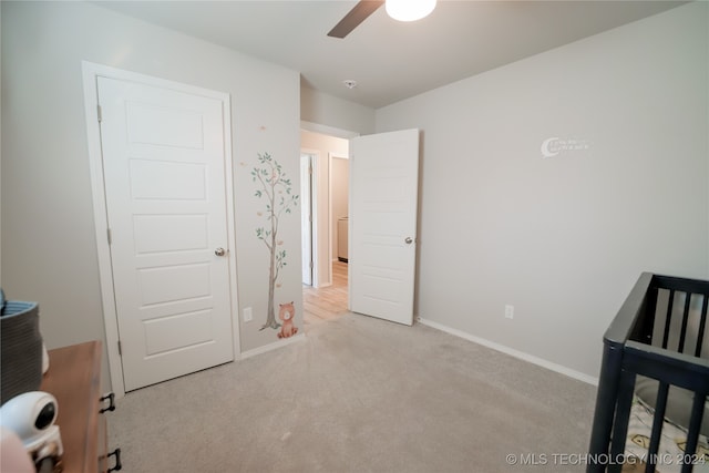 bedroom featuring ceiling fan, light colored carpet, and a crib