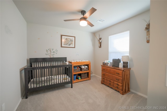 carpeted bedroom featuring ceiling fan and a crib