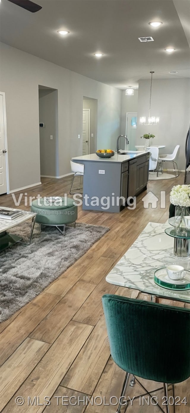 kitchen with pendant lighting, sink, an inviting chandelier, light hardwood / wood-style flooring, and a kitchen island with sink