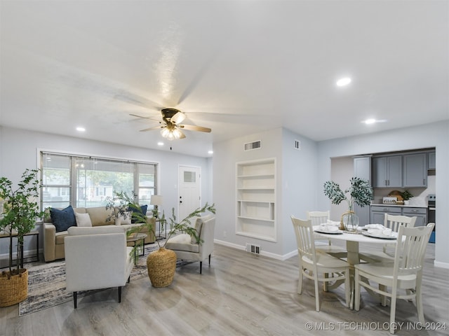 living room with built in shelves, ceiling fan, and light wood-type flooring