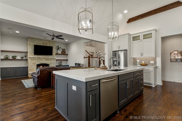 kitchen with a center island with sink, a stone fireplace, white cabinetry, decorative light fixtures, and dark hardwood / wood-style floors