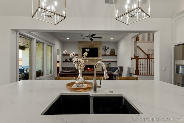 kitchen featuring hanging light fixtures, crown molding, sink, light stone countertops, and a fireplace