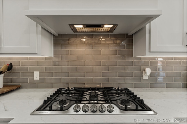 kitchen with stainless steel gas stovetop, light stone countertops, decorative backsplash, and white cabinetry