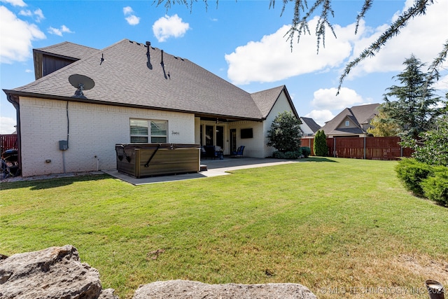 back of house with a hot tub, a patio area, and a lawn