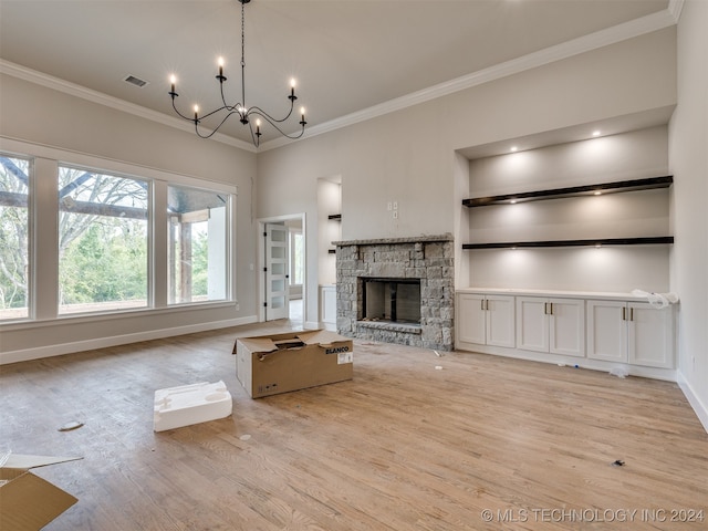 unfurnished living room with light hardwood / wood-style floors, a stone fireplace, crown molding, built in shelves, and a chandelier