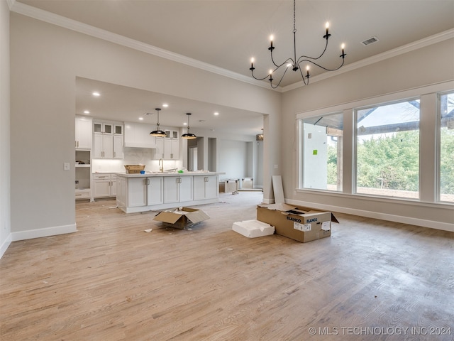 unfurnished living room with light wood-type flooring, ornamental molding, sink, and a notable chandelier