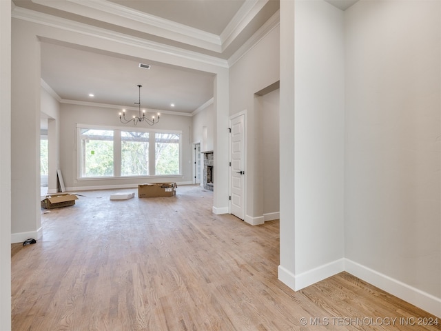 unfurnished living room with ornamental molding, an inviting chandelier, a fireplace, and light hardwood / wood-style floors