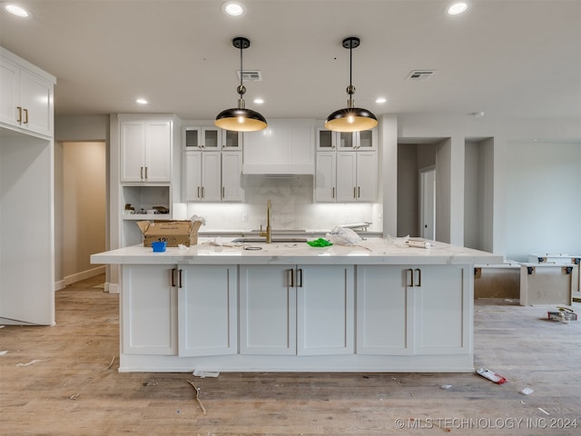 kitchen featuring light wood-type flooring, white cabinetry, hanging light fixtures, and a kitchen island with sink