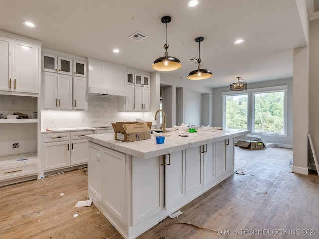 kitchen with light stone counters, pendant lighting, an island with sink, white cabinets, and light hardwood / wood-style floors