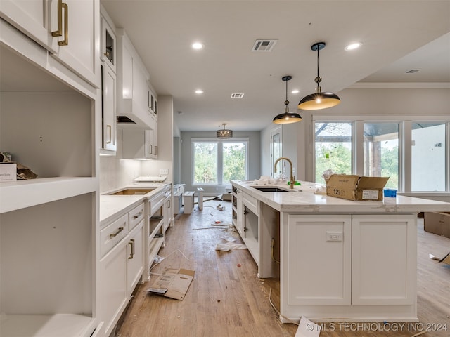 kitchen with sink, pendant lighting, an island with sink, and white cabinets