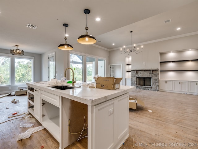 kitchen featuring decorative light fixtures, a kitchen island with sink, light wood-type flooring, and white cabinetry