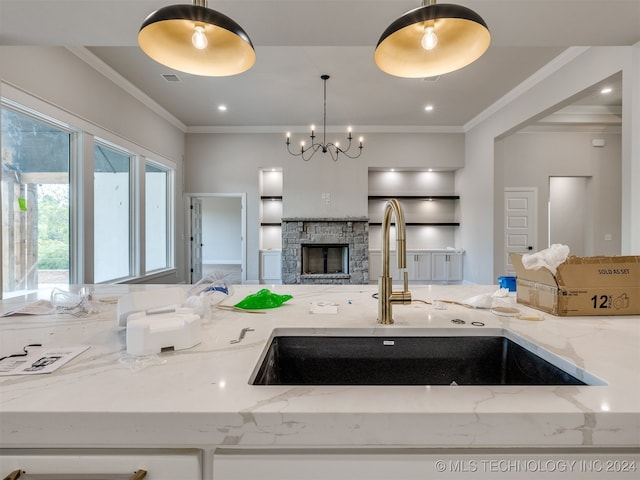 kitchen with pendant lighting, light stone counters, crown molding, and sink