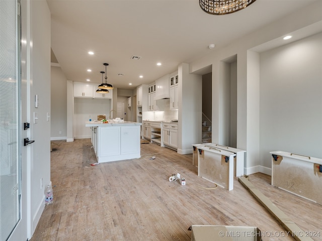 kitchen with sink, an island with sink, white cabinetry, hanging light fixtures, and light hardwood / wood-style flooring