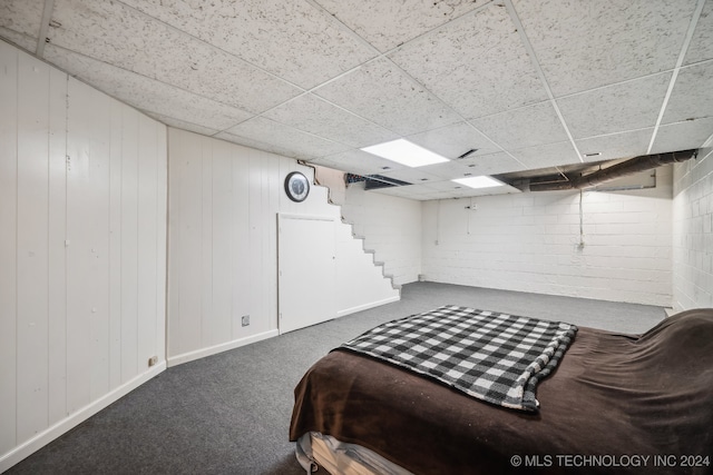 bedroom with carpet, a drop ceiling, and wood walls