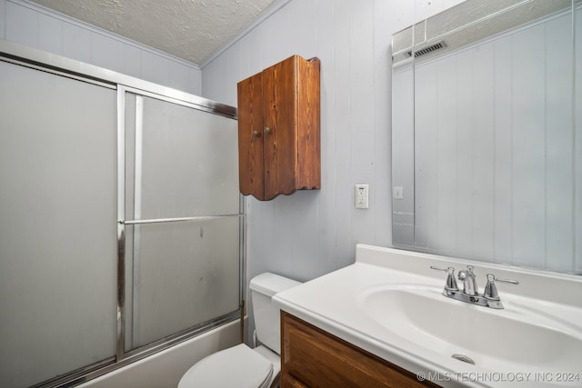 full bathroom with vanity, a textured ceiling, wooden walls, bath / shower combo with glass door, and toilet