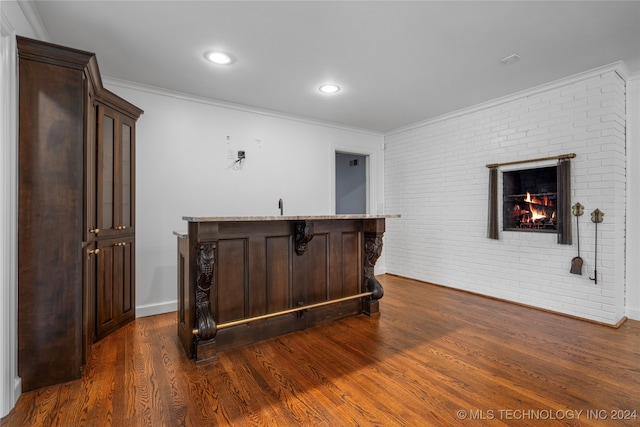 bar with dark wood-type flooring, brick wall, a fireplace, crown molding, and dark brown cabinetry