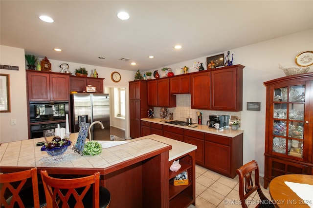 kitchen featuring an island with sink, black appliances, tile countertops, and backsplash