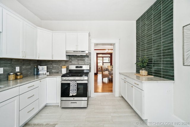 kitchen with tasteful backsplash, white cabinets, light stone counters, and stainless steel gas range oven