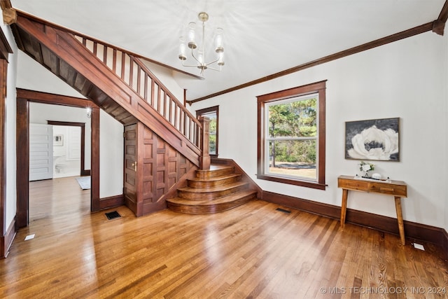 stairs featuring wood-type flooring, ornamental molding, and an inviting chandelier