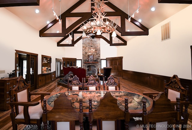 dining room featuring high vaulted ceiling, a stone fireplace, beamed ceiling, wood-type flooring, and an inviting chandelier