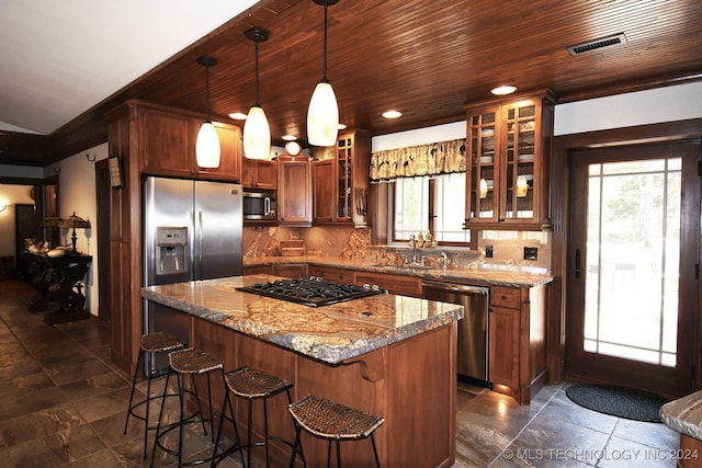 kitchen featuring light stone counters, pendant lighting, appliances with stainless steel finishes, a center island, and decorative backsplash