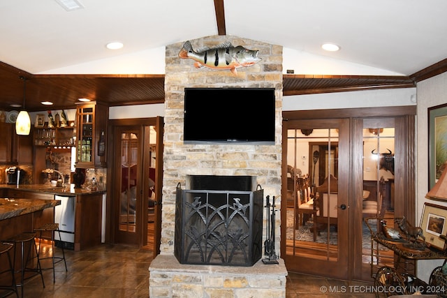 living room with vaulted ceiling with beams, a stone fireplace, and wet bar