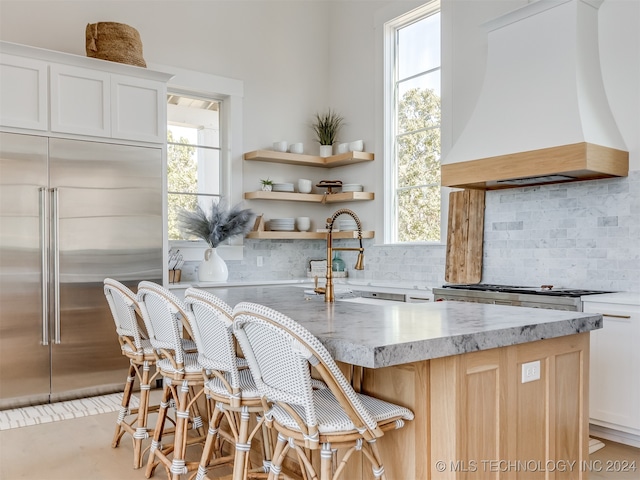 kitchen with sink, stainless steel built in fridge, a kitchen breakfast bar, white cabinets, and custom range hood