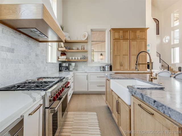 kitchen featuring high end stove, white cabinets, decorative backsplash, light hardwood / wood-style flooring, and premium range hood