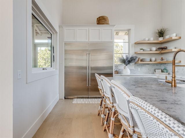 kitchen with sink, built in fridge, white cabinetry, light hardwood / wood-style floors, and light stone counters