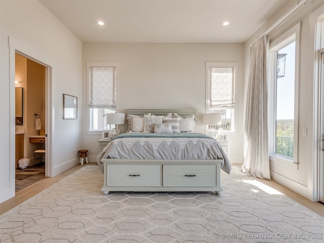 bedroom featuring multiple windows, light wood-type flooring, and ensuite bath