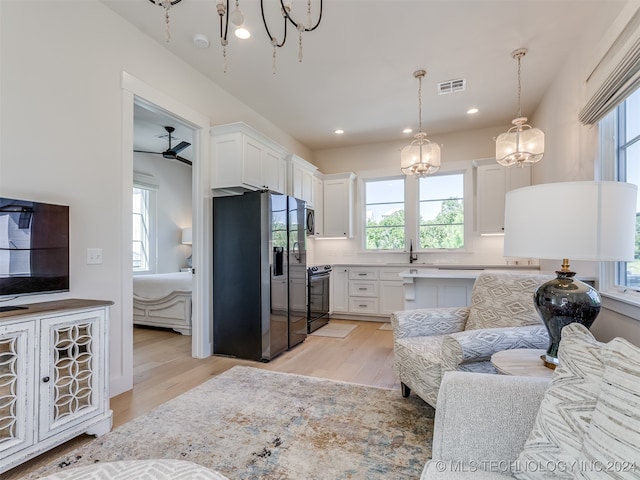 kitchen with hanging light fixtures, stainless steel appliances, light wood-type flooring, white cabinetry, and ceiling fan with notable chandelier