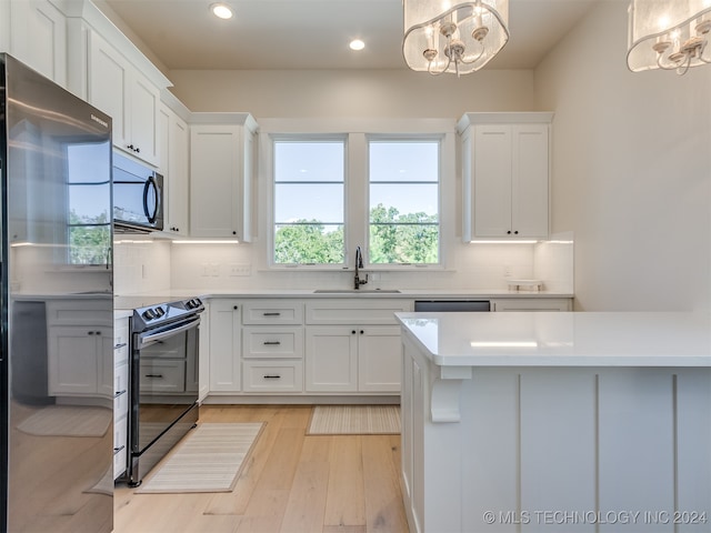 kitchen with sink, black appliances, white cabinetry, and hanging light fixtures