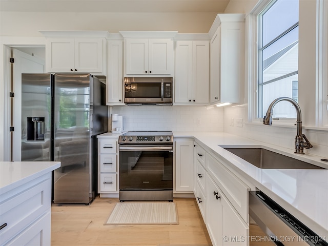 kitchen with backsplash, sink, white cabinets, appliances with stainless steel finishes, and light hardwood / wood-style floors