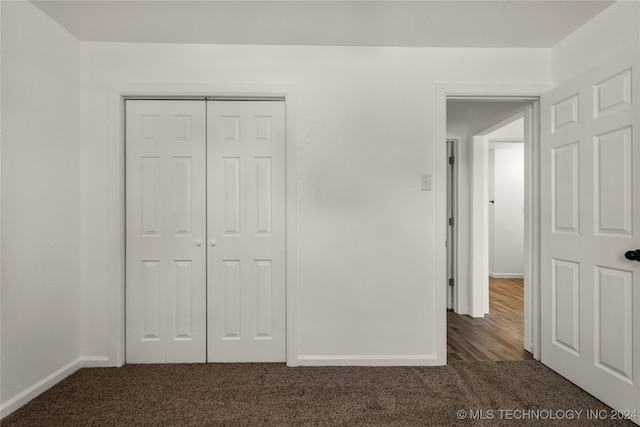 unfurnished bedroom with dark carpet and a closet