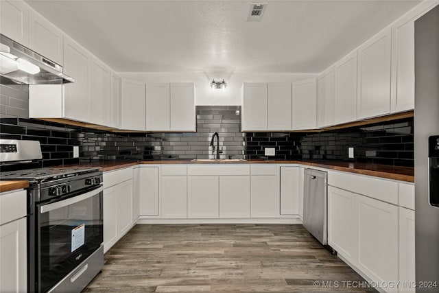 kitchen featuring wooden counters, stainless steel gas range oven, sink, white cabinetry, and range hood