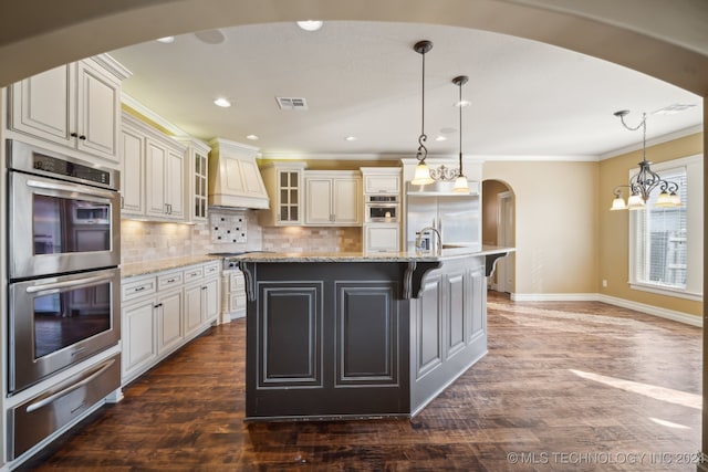 kitchen featuring light stone counters, hanging light fixtures, a center island with sink, stainless steel appliances, and dark hardwood / wood-style floors