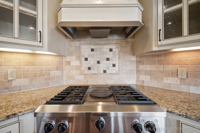 kitchen with decorative backsplash, white cabinetry, light stone counters, stainless steel stove, and custom exhaust hood