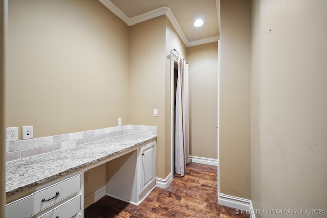 interior space with light stone countertops, built in desk, ornamental molding, and dark hardwood / wood-style flooring