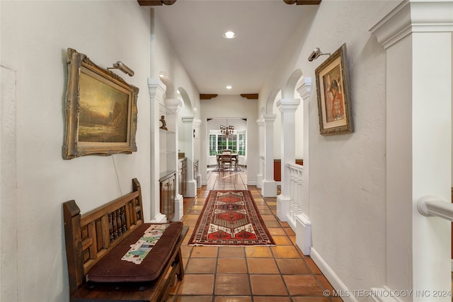 corridor with a notable chandelier, ornate columns, and dark tile patterned floors