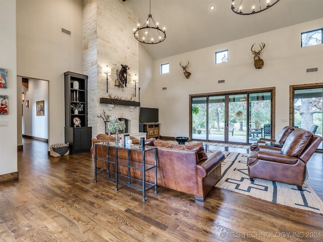 living room with a stone fireplace, dark wood-type flooring, a high ceiling, and a chandelier