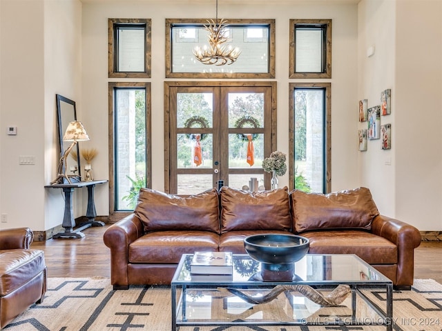 living room featuring an inviting chandelier, light hardwood / wood-style flooring, a high ceiling, and french doors