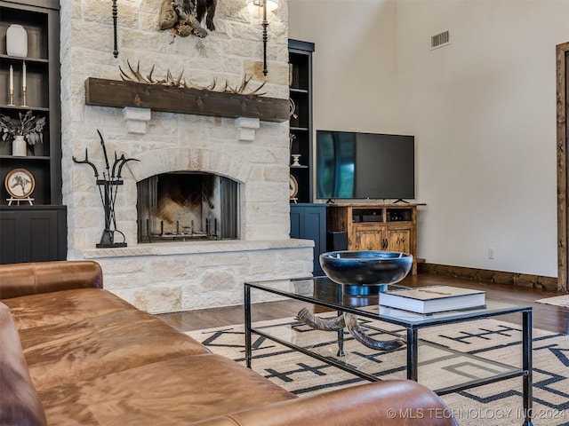 living room with hardwood / wood-style flooring, built in shelves, and a stone fireplace