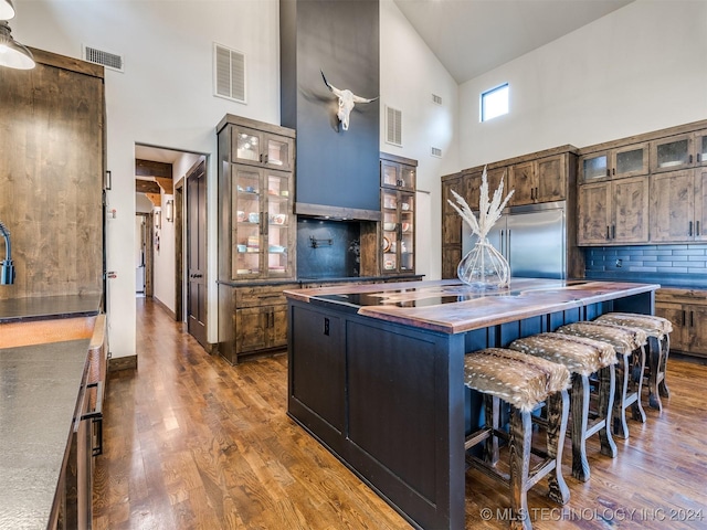 kitchen with decorative backsplash, a kitchen breakfast bar, stainless steel built in fridge, high vaulted ceiling, and an island with sink