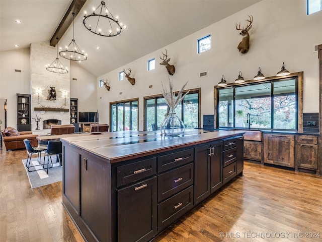 kitchen with beam ceiling, a center island, a stone fireplace, high vaulted ceiling, and pendant lighting