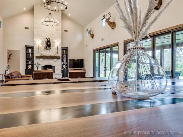 interior space with a stone fireplace, high vaulted ceiling, and an inviting chandelier